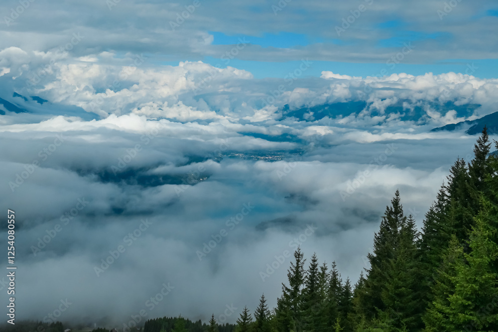 Evergreen trees frame a stunning aerial view of Lake Millstatt, partially obscured by a sea of clouds clinging to valleys below in Carinthia, Austria. Beauty and tranquility of the Alps. Wanderlust Evergreen trees frame a stunning aerial view of Lake Millstatt, partially obscured by a sea of clouds clinging to valleys below in Carinthia, Austria. Beauty and tranquility of the Alps. Wanderlust