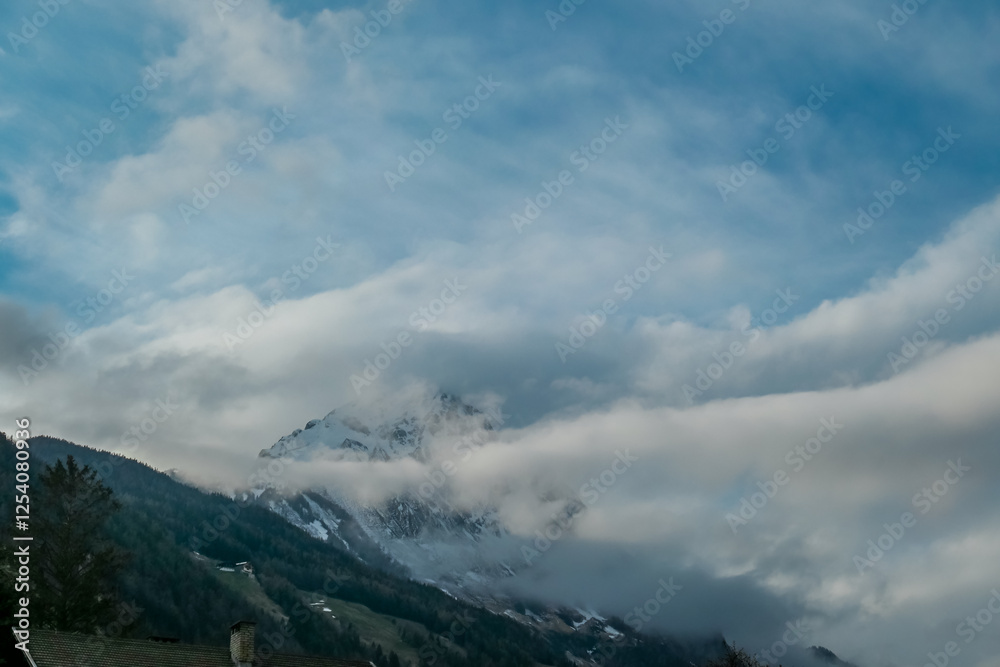Dramatic mountain peak, partially shrouded in swirling clouds, dominates the sky above the village of Matrei in East Tyrol, Austria. Seeking remote scenery and fresh mountain air in Austrian Alps Dramatic mountain peak, partially shrouded in swirling clouds, dominates the sky above the village of Matrei in East Tyrol, Austria. Seeking remote scenery and fresh mountain air in Austrian Alps