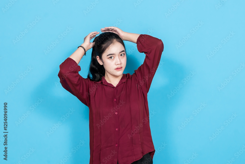 Confident woman wearing a red shirt poses elegantly against a blue background, displaying serene emotions. Confident woman wearing a red shirt poses elegantly against a blue background, displaying serene emotions.