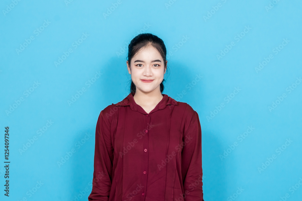 Cheerful young woman smiling confidently and standing against a blue background, expressing positivity. Cheerful young woman smiling confidently and standing against a blue background, expressing positivity.
