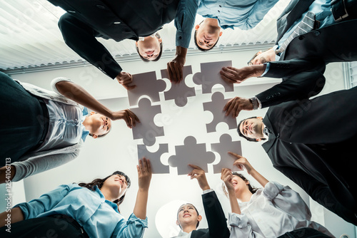 Multiethnic business people holding jigsaw pieces and merge them together as effective solution solving teamwork, shared vision and common goal combining diverse talent. Below view. Habiliment photo