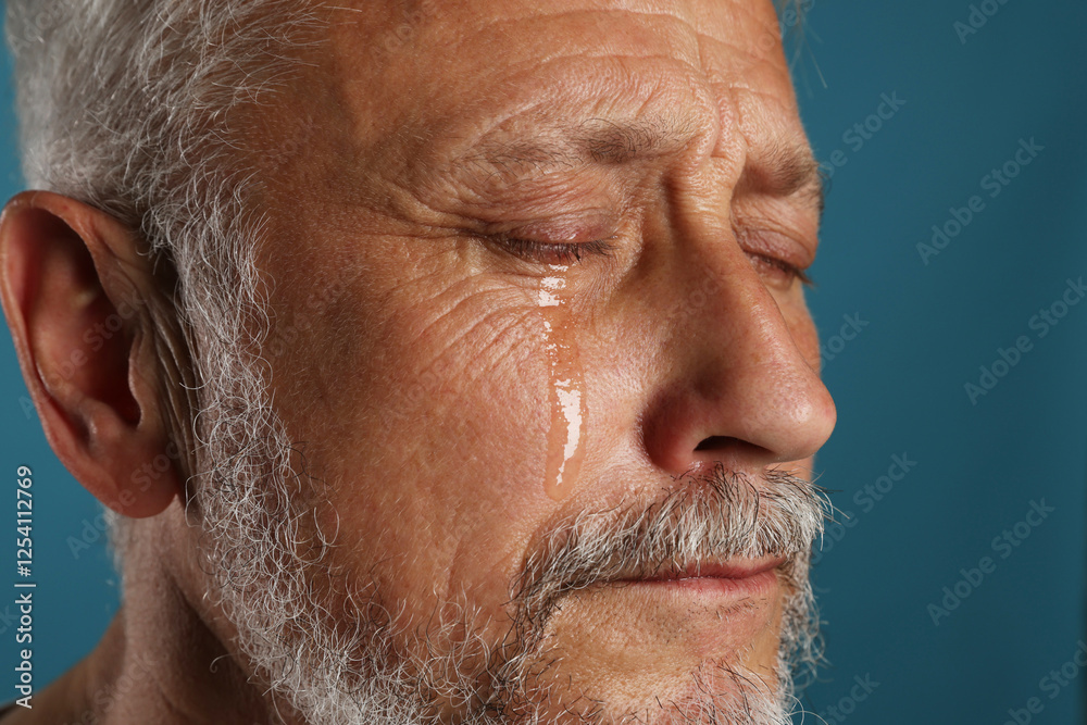 Fototapeta premium Sad senior man crying on blue background, closeup