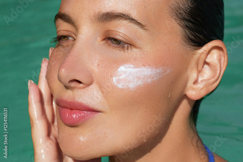 Spf, sunblock skincare cosmetics treatments. Beauty portrait of a woman with dewy skin applying sunscreen cream to her cheek on the pool or sea, highlighting hydration and sun protection.  photo