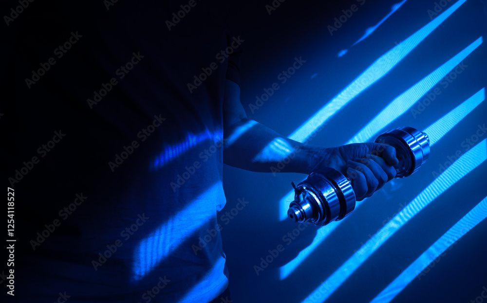 Athlete lifting dumbbell in dark blue gym with striped shadows