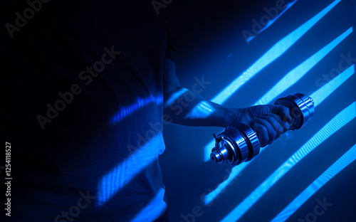 Obraz na płótnie Athlete lifting dumbbell in dark blue gym with striped shadows w salonie