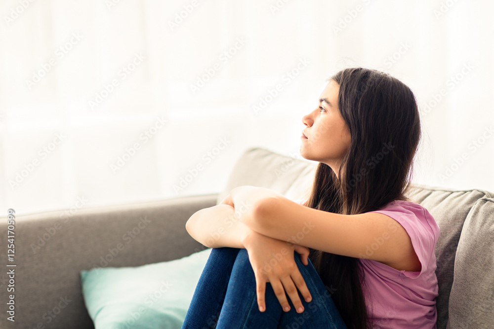 Teen depression concept. Stressed Indian teenage girl sitting on couch at home, looking out window, suffering from lack of communication, feeling upset and lonely during covid lockdown Teen depression concept. Stressed Indian teenage girl sitting on couch at home, looking out window, suffering from lack of communication, feeling upset and lonely during covid lockdown