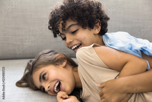 Two adorable little children, siblings or close friends lying on comfortable couch, laughing, enjoying fun and playful moments together, having joyful expressions, close up. Family bonding, playtime