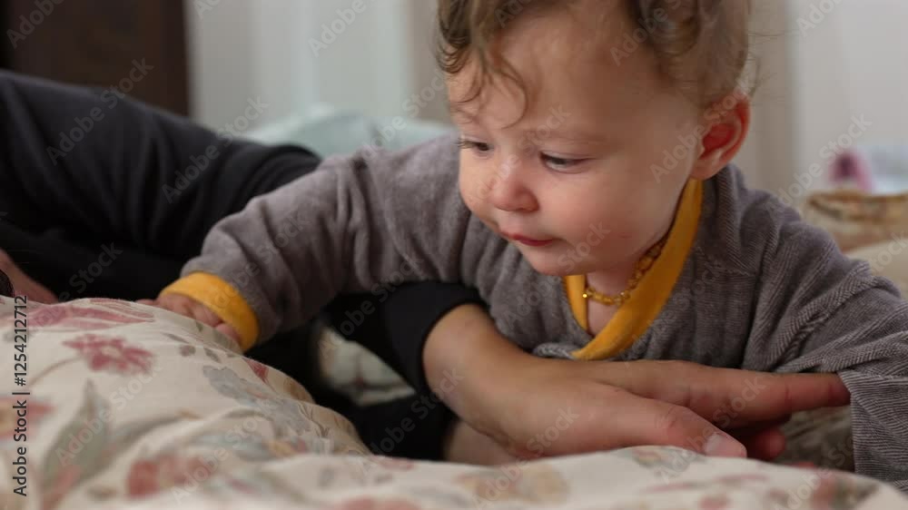 Baby reaching out with curious expression while lying on bed, supported by mother’s arm, exploring surroundings, tender family bonding moment, cozy indoor setting, early development Baby reaching out with curious expression while lying on bed, supported by mother’s arm, exploring surroundings, tender family bonding moment, cozy indoor setting, early development