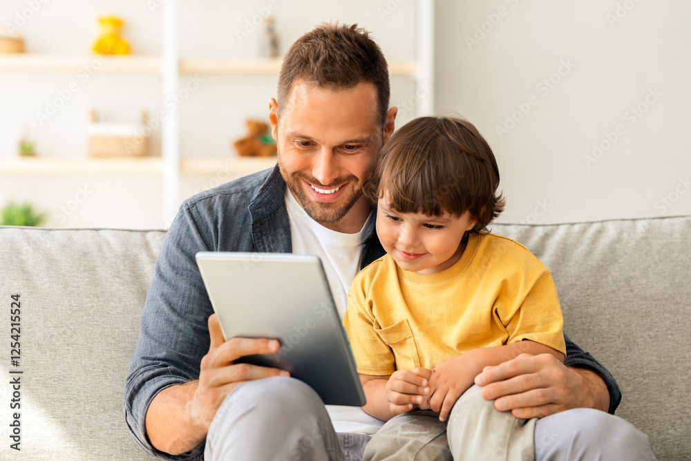Child development content. Young positive father showing digital tablet to his cute little son, kid enjoying educational show online, sitting on sofa ta home Child development content. Young positive father showing digital tablet to his cute little son, kid enjoying educational show online, sitting on sofa ta home