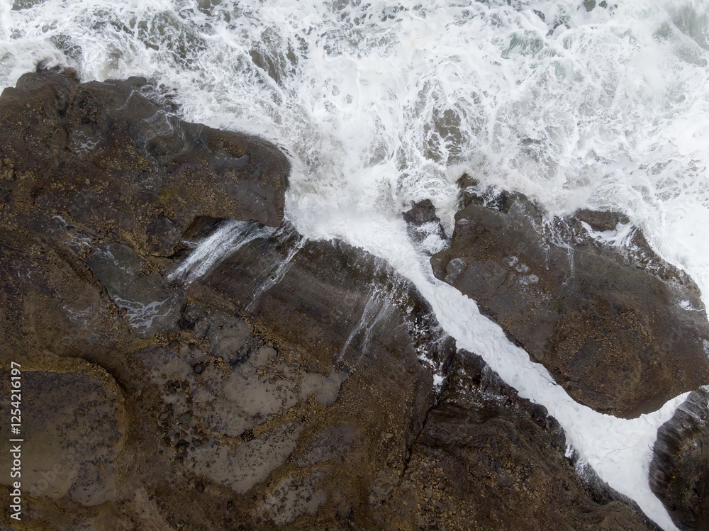 Naklejka premium Powerful waves crash against rugged coastal rocks. Ocean spray creates a foamy white line. Coastal erosion. Piha, Auckland, New Zealand