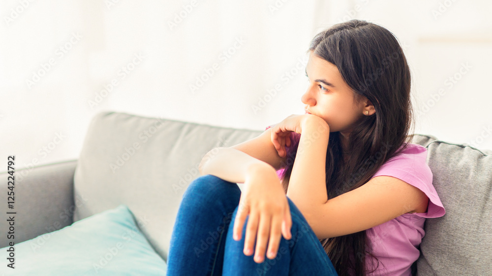 Stressed Indian teenage girl sitting on sofa at home, looking aside, feeling upset and lonely, suffering from lack of communication during covid lockdown. Teen depression concept Stressed Indian teenage girl sitting on sofa at home, looking aside, feeling upset and lonely, suffering from lack of communication during covid lockdown. Teen depression concept