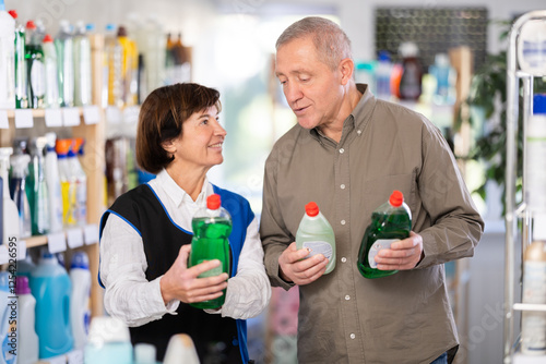 Elderly woman seller offers dishwashing detergent to elderly man buyer in household chemicals store