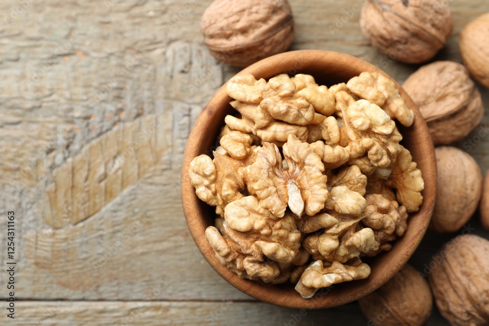 Peeled walnuts in bowl and whole ones on wooden table, flat lay. Space for text Peeled walnuts in bowl and whole ones on wooden table, flat lay. Space for text
