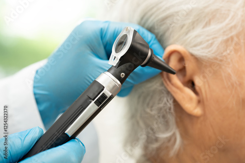 Audiologist or ENT doctor use otoscope checking ear of asian senior woman patient treating hearing loss problem.