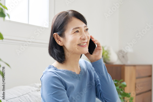 Fotografie スマホで電話する中年女性　リビング