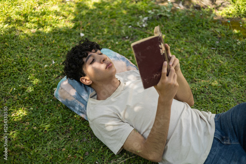 A person relaxing in the park, enjoying their favorite novel. Perfect for themes of leisure, reading, relaxation, and outdoor enjoyment.