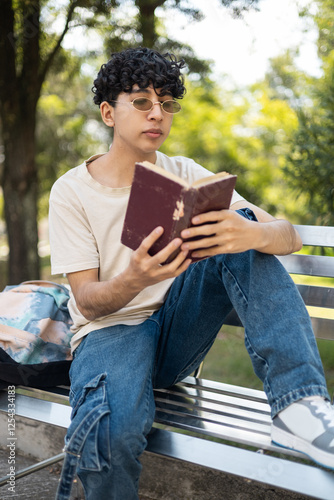  A young person reading a book on a park bench, enjoying the peaceful atmosphere and nature around them. Perfect for themes of leisure, outdoor reading, relaxation, and tranquility.