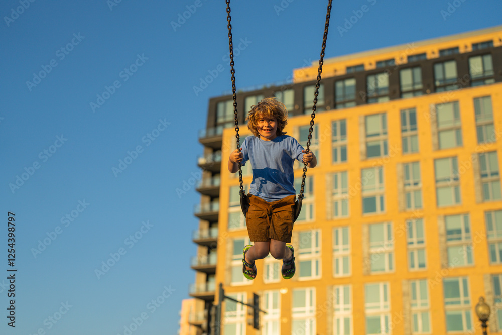 Kid swinging on chain swing on city kids playground. Swing ride. Cute child having fun on a swing on summer sky background. Kids playing in park. Blonde little boy swings at kid playground. Kid swinging on chain swing on city kids playground. Swing ride. Cute child having fun on a swing on summer sky background. Kids playing in park. Blonde little boy swings at kid playground.