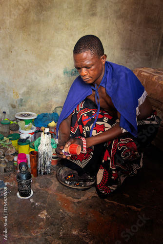 African village sangoma wearing a blue cloak and traditional attire, performing a spiritual ritual indoors, surrounded by herbs, bones, and candles, Botswana, traditional healer, ancestral connection photo