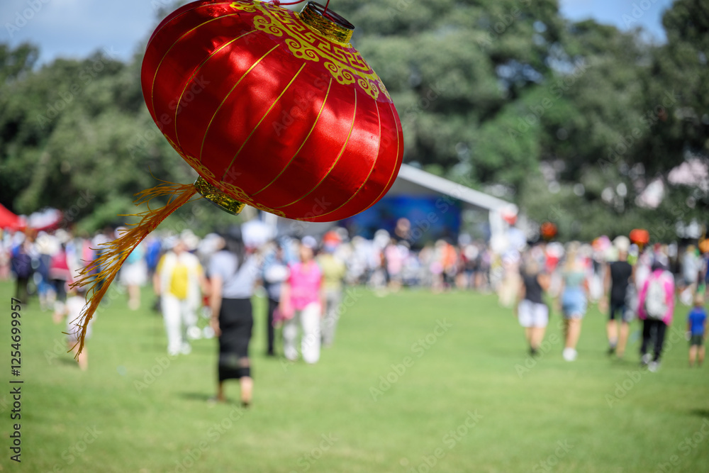 Red lanterns hanging under the Pohutukawa trees. Unrecognizable crowd of people celebrating Chinese New Year. Auckland.