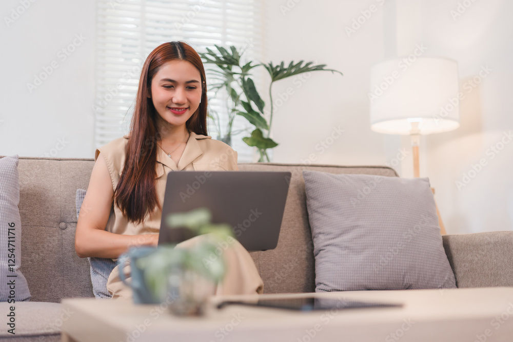 Woman smiling while working on laptop in cozy living room with natural light. Woman smiling while working on laptop in cozy living room with natural light.
