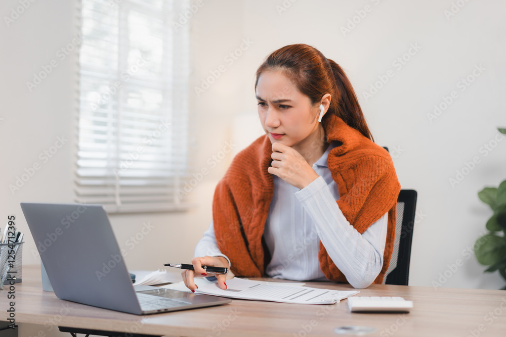 Focused woman working at desk with laptop, documents, and wearing wireless earbuds in bright office. Focused woman working at desk with laptop, documents, and wearing wireless earbuds in bright office.