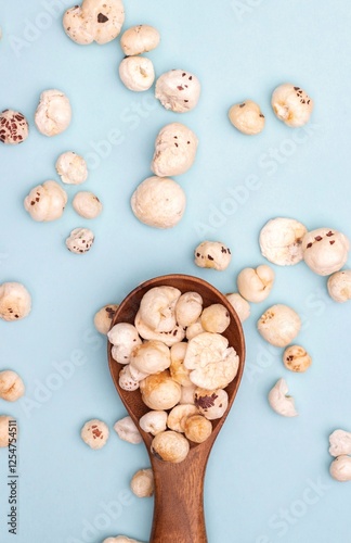 Top View of Makhana or Fox Nut in a Wooden Spoon Isolated on Light Blue Background with Copy Space in Vertical Orientation, Also Known as Lotus Seed Pop, Euryale Ferox or Gorgon Nut