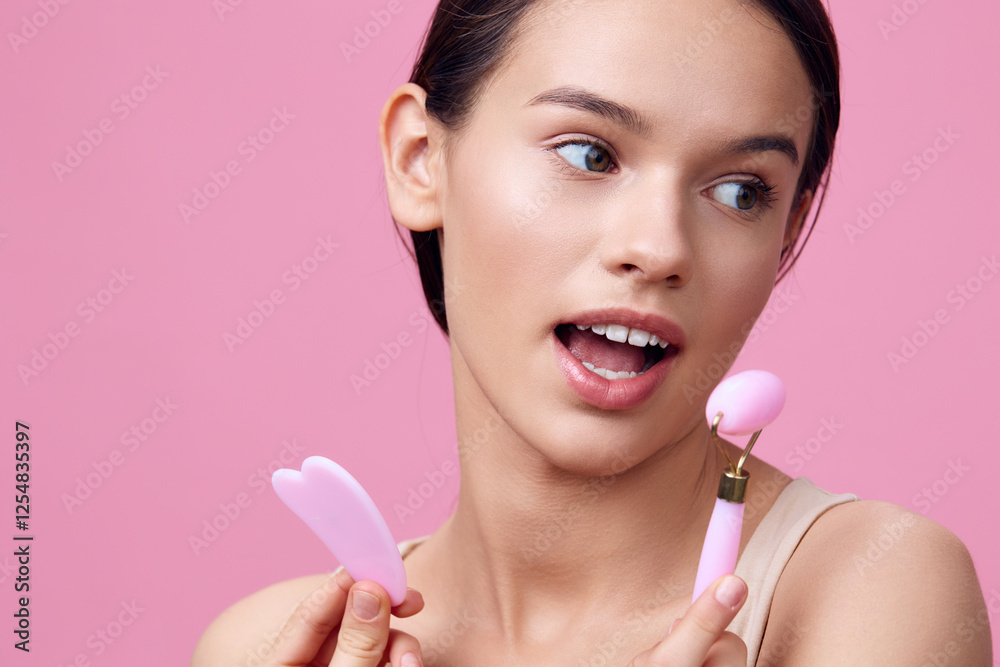 Young woman showcasing beauty tools against a pink backdrop, expressing excitement and curiosity about skincare techniques Young woman showcasing beauty tools against a pink backdrop, expressing excitement and curiosity about skincare techniques