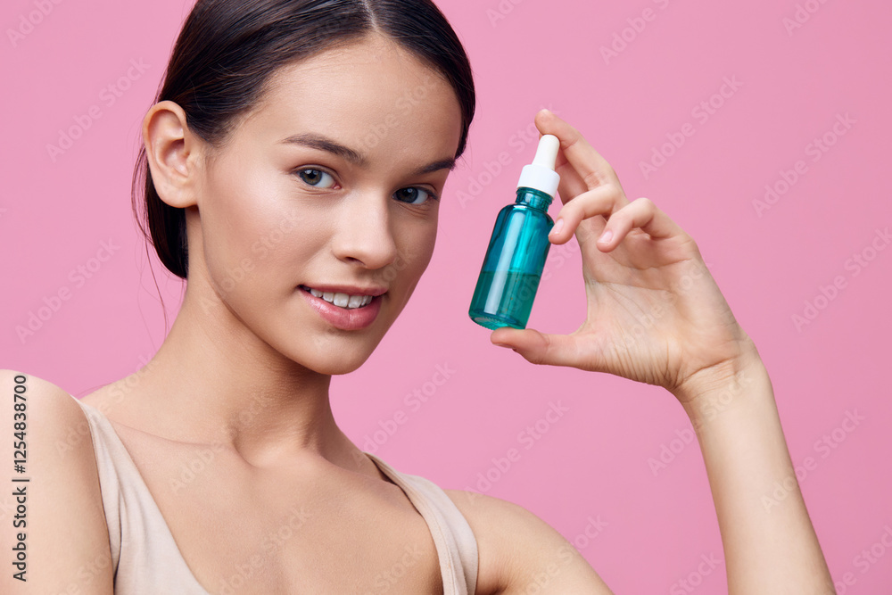 Young woman holding a blue serum bottle, smiling, against a pink background, showcasing beauty and skincare concepts, ideal for wellness and cosmetics themes Young woman holding a blue serum bottle, smiling, against a pink background, showcasing beauty and skincare concepts, ideal for wellness and cosmetics themes