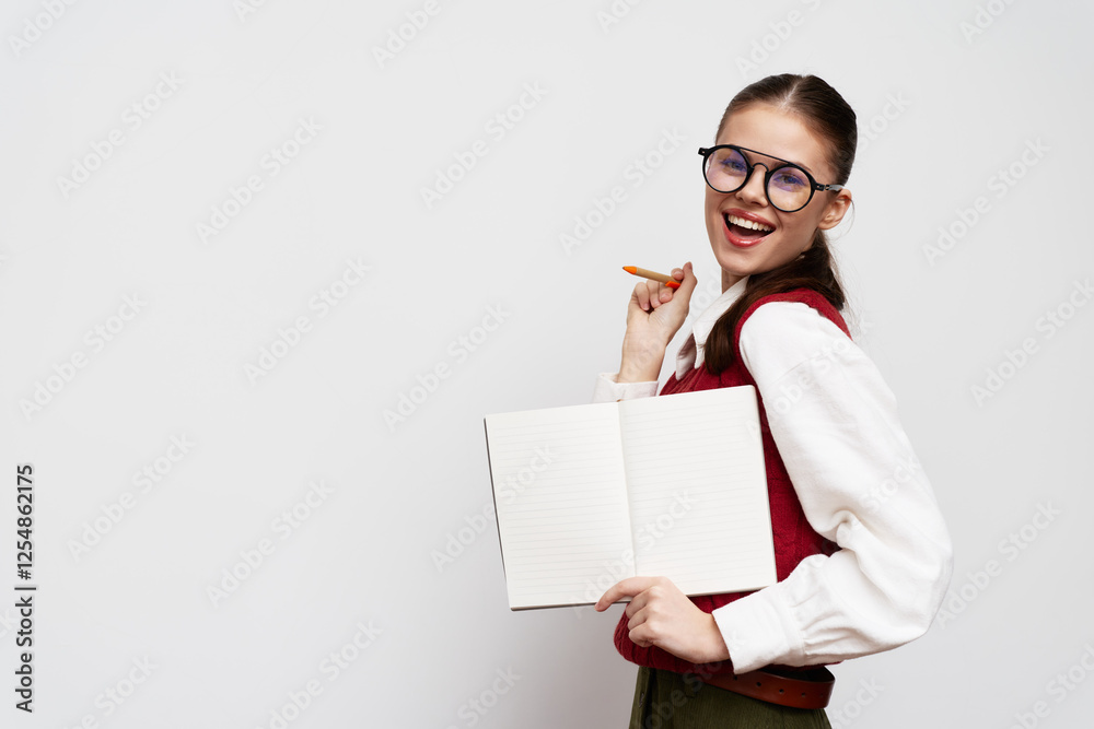Cheerful student with glasses holding an open notebook and a pencil against a neutral background She s wearing a red vest and showing a confident smile Perfect for educational themes Cheerful student with glasses holding an open notebook and a pencil against a neutral background She s wearing a red vest and showing a confident smile Perfect for educational themes