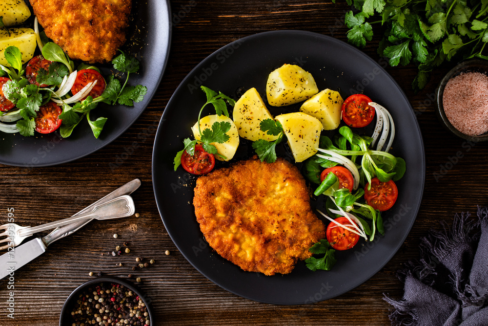 Breaded fried pork chop with fresh vegetable salad and potatoes on wooden table	
