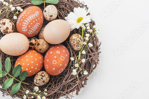 Easter nest with hand-painted eggs and quail eggs on a light background. A rustic spring composition with natural elements, fresh greenery and floral details. photo