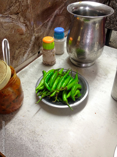 Bowl of green chillies, Salt and pepper shakers, pitcher of water and spicy mango chutney on table of old local cafe or diner in Dheli, India. Wheathered cafe, full of life and costumers. photo