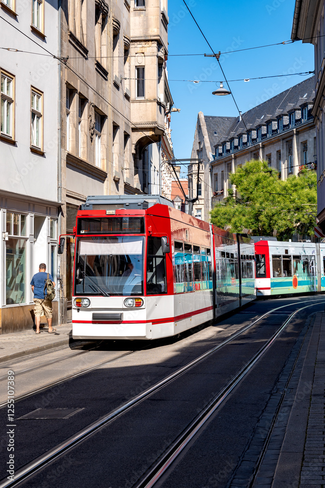 Fototapeta premium A vibrant scene from Erfurt, Thuringia, featuring a modern red and white tram navigating through the city's historic streets