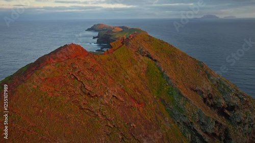 Dramatic aerial drone coastal cliff shot at sunset, revealing vibrant ocean and rugged volcanic terrain under a glowing sky. Miradouro Ponta do Furado Madeira.