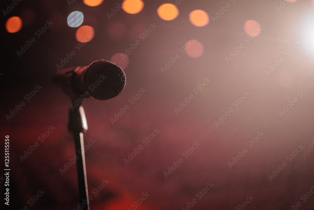 Obraz premium A microphone on a stand with dramatic stage lighting and blurred bokeh lights in the background, creating a moody atmosphere..