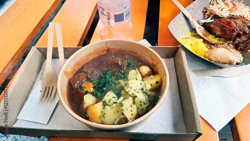 Tourists eating takeaway Fast food on a street bench. Box containing Hungarian beef stew with parsley potato