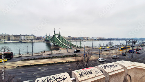 View of the road and tramway lines of Pest with the Liberty Bridge seen from the Gellert Hill rock chapel at a winter sunset. Buda cityscape on the other side of the Danube River, Budapest, Hungary.