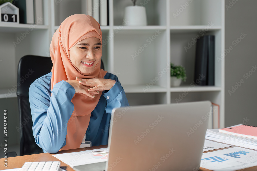 Muslim woman smiling while engaging with her laptop in a modern office setting. Muslim woman smiling while engaging with her laptop in a modern office setting.