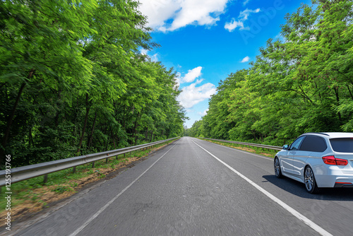 A sleek white car speeds along a scenic highway surrounded by lush green trees under a bright blue sky with scattered clouds, creating a sense of motion and adventure.