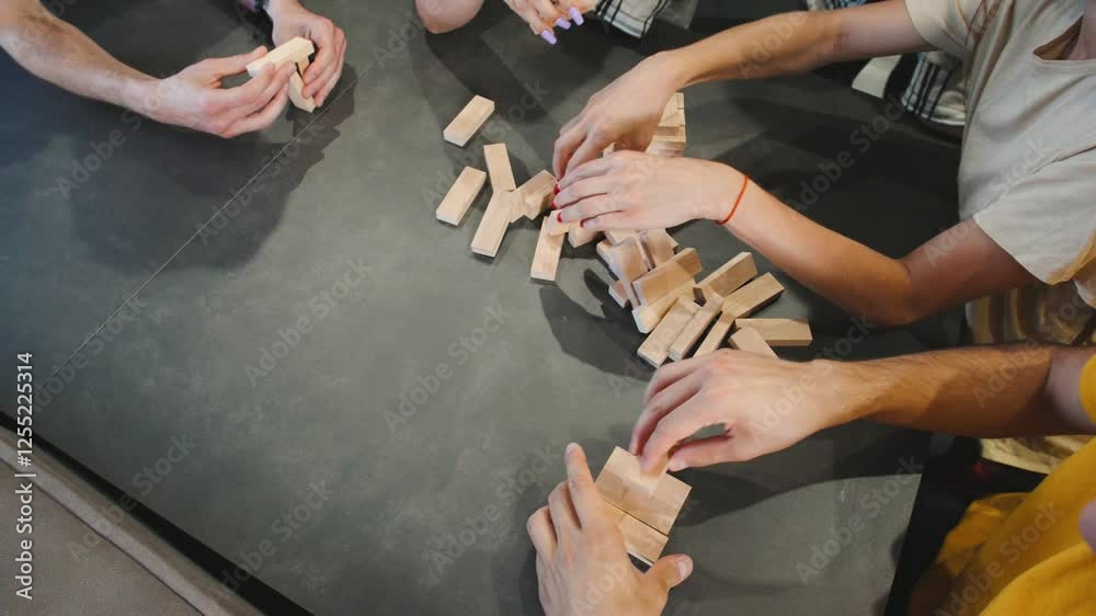 Group of friends engaged in a lively game of stacking blocks of Jenga at a cozy gathering in a stylish indoor space during the afternoon