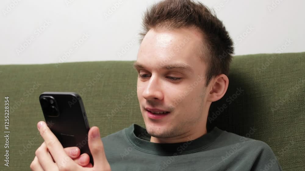 Young man sitting on a couch engaged in conversation on a smartphone Young man sitting on a couch engaged in conversation on a smartphone