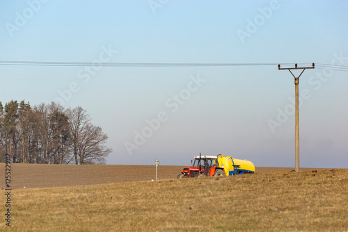 Obraz na płótnie A tractor drives along a road in the countryside on a cold winter morning. w salonie