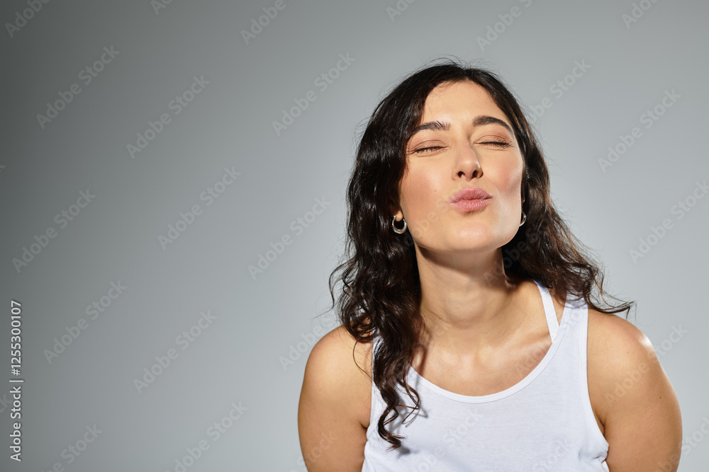 Obraz premium Joyful brunette woman blowing a kiss in a stylish studio setting