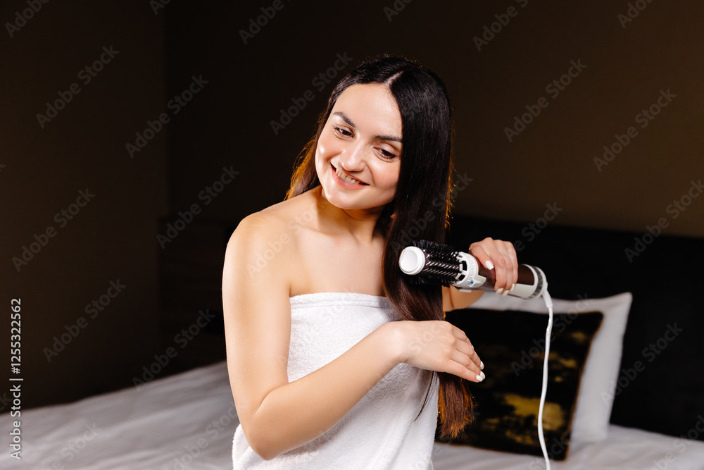 A beautiful woman in bath towel standing in room dries and styles her hair with a hair dryer comb. Morning routine. A beautiful woman in bath towel standing in room dries and styles her hair with a hair dryer comb. Morning routine.