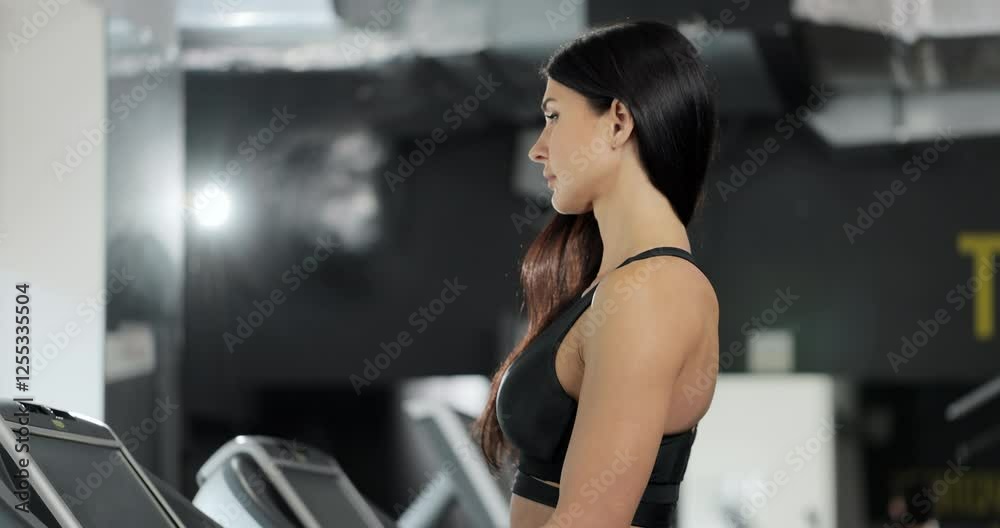 Attractive caucasian girl is starting to run on the treadmill in the sport gym. Portrait of attractive girl athlete training at gym. Sport and healthy lifestyle concept. Attractive caucasian girl is starting to run on the treadmill in the sport gym. Portrait of attractive girl athlete training at gym. Sport and healthy lifestyle concept.