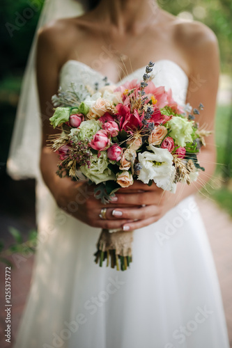 Colorful wedding bouquet with roses, greenery, and wildflowers held by a bride wearing a white wedding dress.

