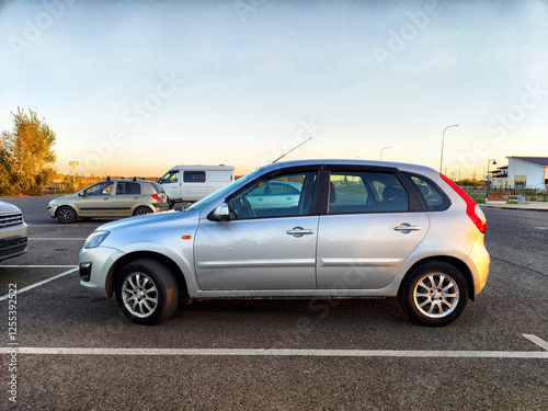 Obraz na plátně Silver hatchback parked in an empty lot during sunset near a quiet residential a