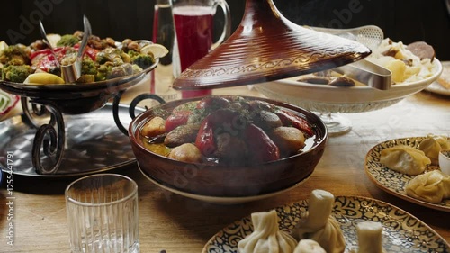 Revealing a steaming tagine surrounded by traditional dishes