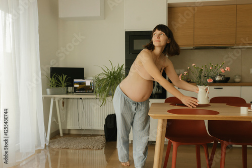 Pregnant woman arranging flower vase on dining table at home